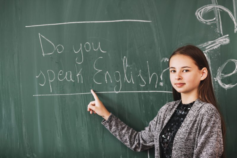 dziewczyna pokazuje palcem zdanie po angielsku na szkolnej tablicy