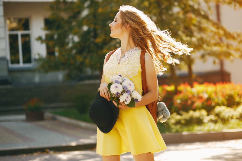 kobieta-w-żółtej-sukience-idzie-ulicą-i-trzyma-białe-kwiaty-w-rękach