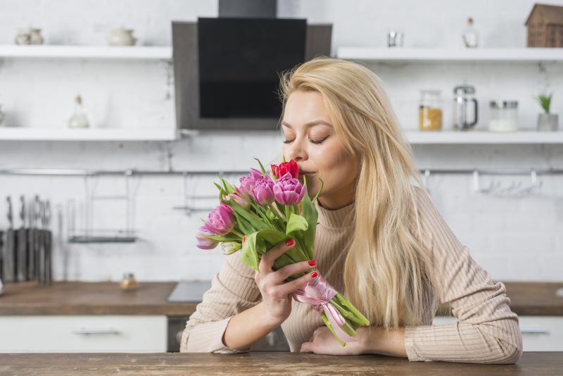 blond kobieta wącha bukiet róż i siedzi w kuchni