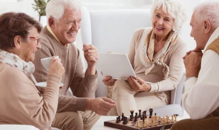 grupa starszych osób siedzi w salonie i gra w szachy